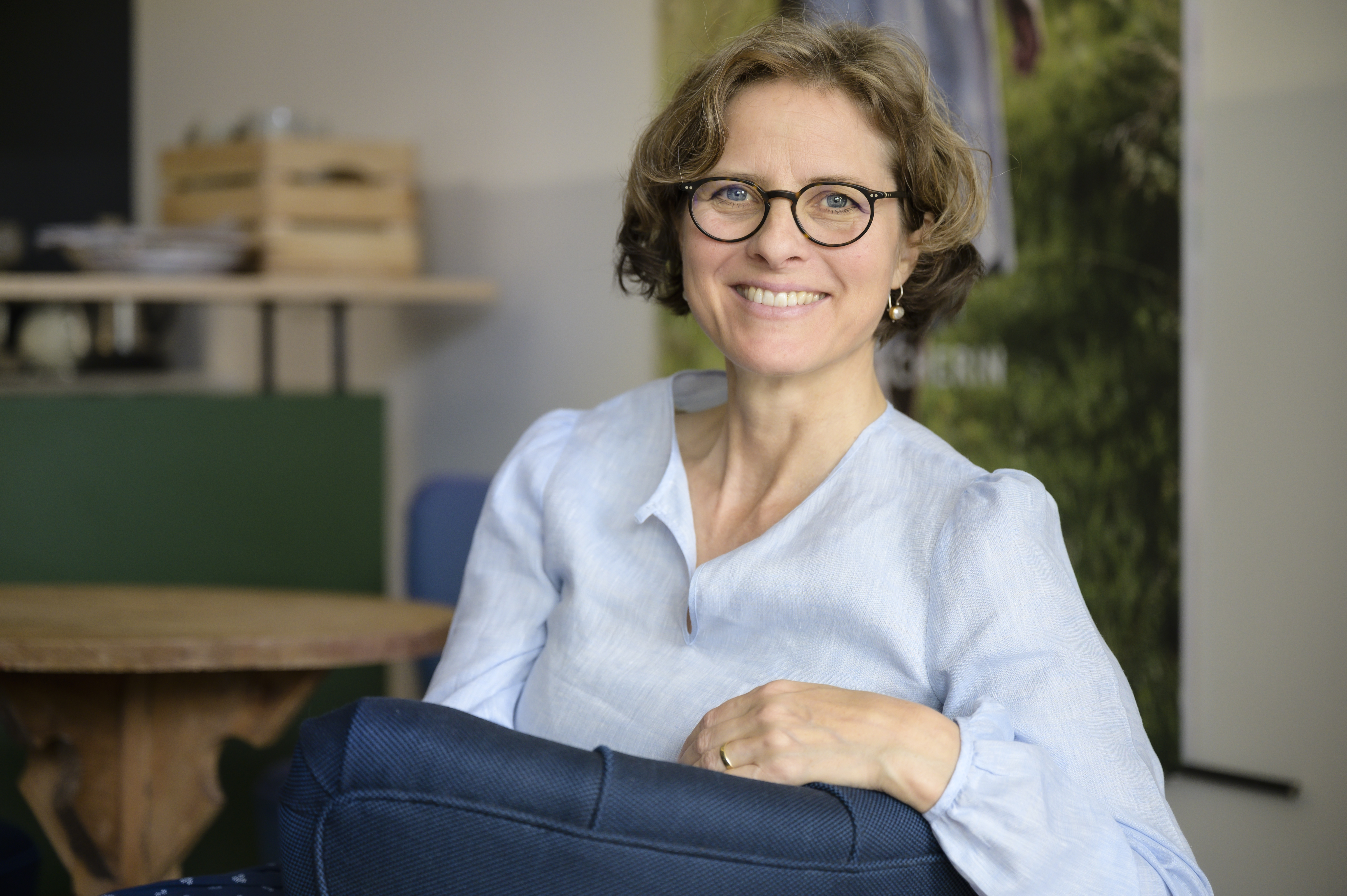 Caroline sitzend in die Kamera schauend in ihrem Büro im Hintergrund Tisch und Büromöbel
