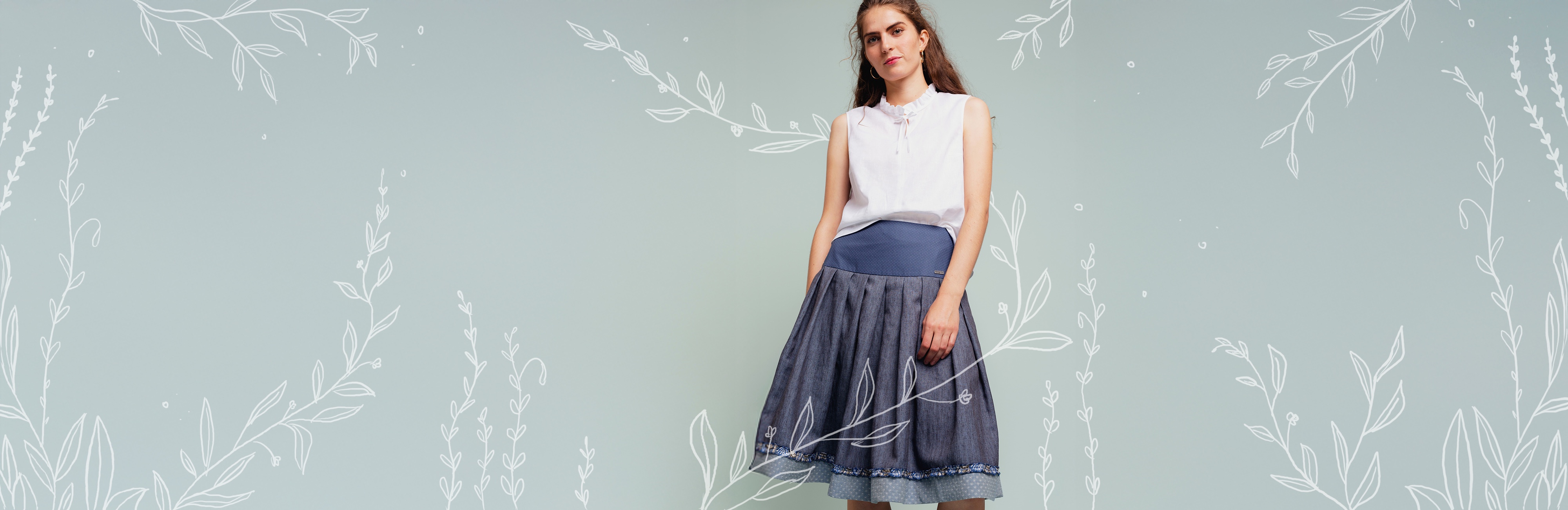 Studiobild von Model mit blauem Klassiker und weißer Bluse. Grafische Rankenelemete in weiß