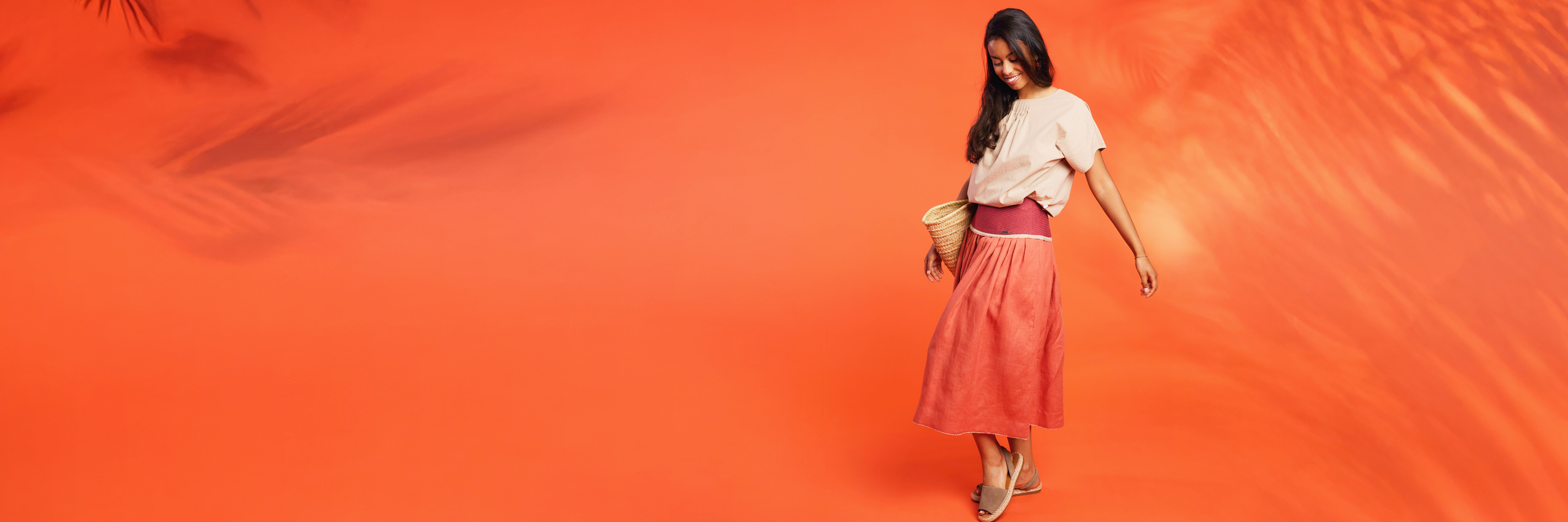 tropisches Gefühl im Studio, im mediterranen Outfit aus beige und rotorange Rock was Model Alma mit einem Strohkorb trägt.