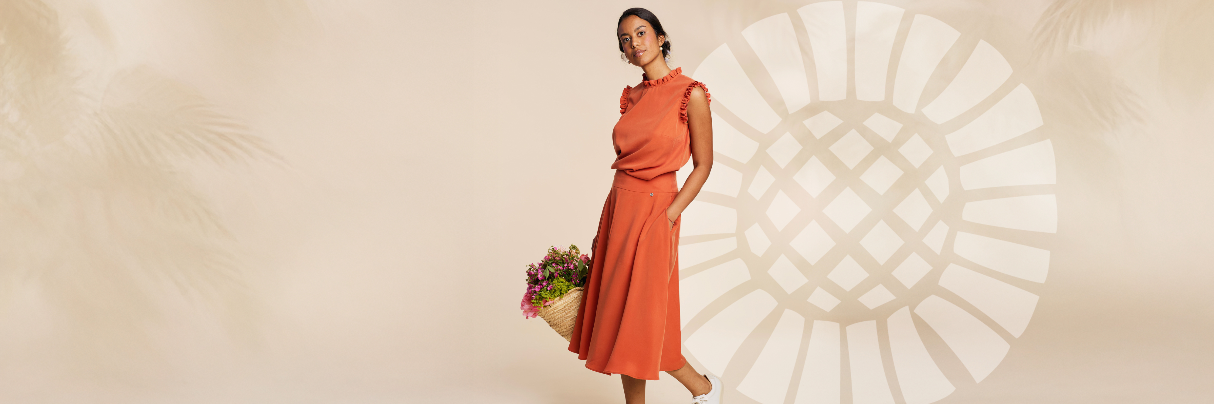 Model trägt oranges Outfit aus Flügelärmelbluse und Rock - im Hintergrund Logoblume von Rockmacherin